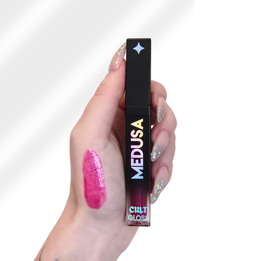 Hand holding a 'MEDUSA' lip gloss with a visible color swatch on the skin.