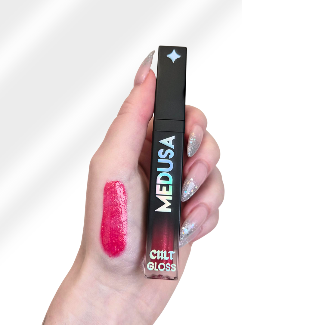 Hand holding a lip gloss with 'MEDUSA' and 'CMT GLOSS' branding on a white background