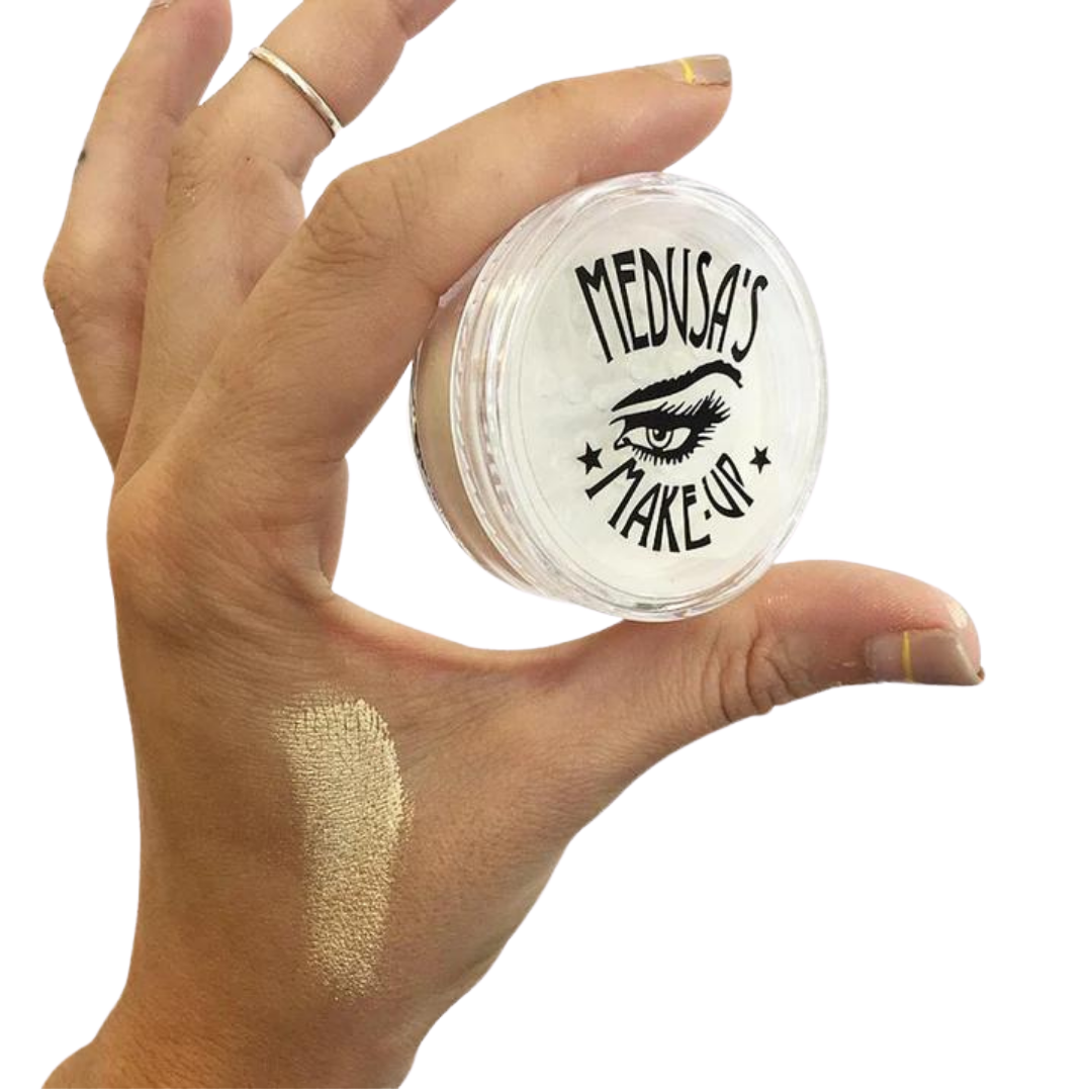Hand holding a jar of 'Medusa's Makeup' with a swatch on the skin.