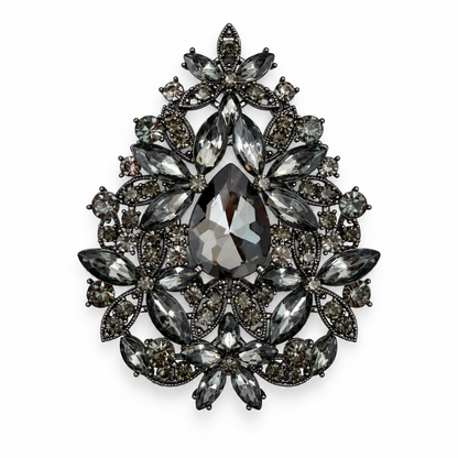 A teardrop-shaped brooch featuring a large faceted dark gray center stone surrounded by multiple marquise and oval-cut gray and smoky crystal stones in a dark metal setting, shown on a plain white background.